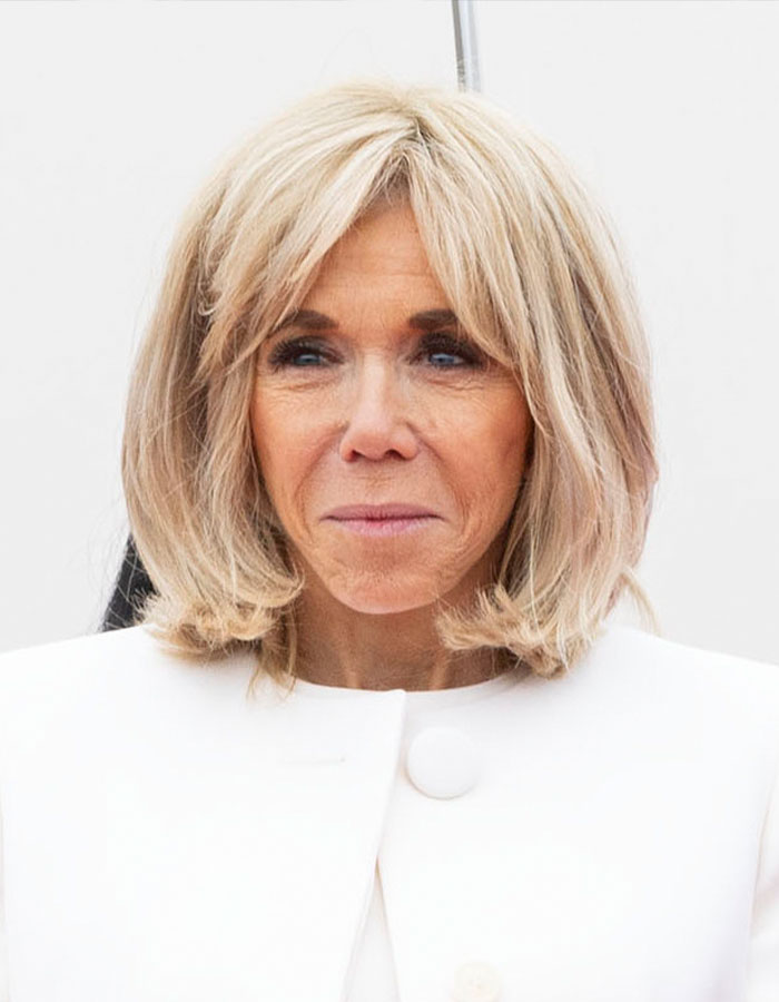 French President's wife in formal attire, facing the camera, with blonde hair.