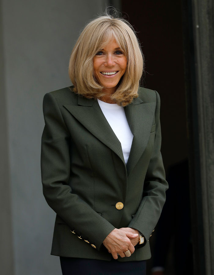 A smiling woman with shoulder-length blond hair wearing a dark green blazer, posing outside.