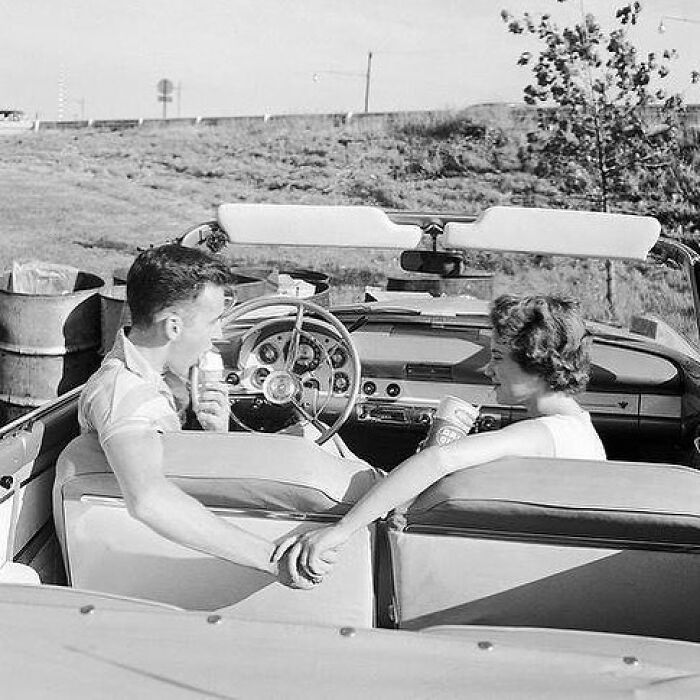 A couple enjoying ice cream and holding hands in a convertible, capturing true happiness on a sunny day.