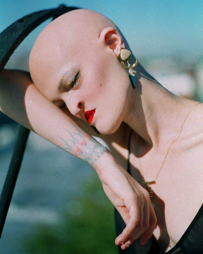 Unique model with bold makeup and statement earrings, posing artistically outdoors.