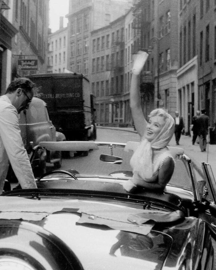 Woman in a convertible, smiling and waving with joy on a city street, capturing true happiness.
