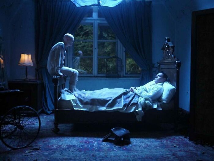 Unique model Melanie Gaydos in a dimly lit room, sitting on a bed, creating a mysterious atmosphere.