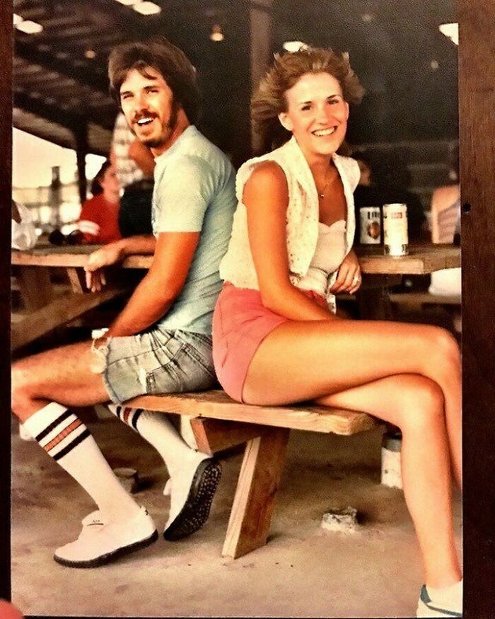 A couple laughing and sitting back-to-back on a picnic bench, capturing true happiness.