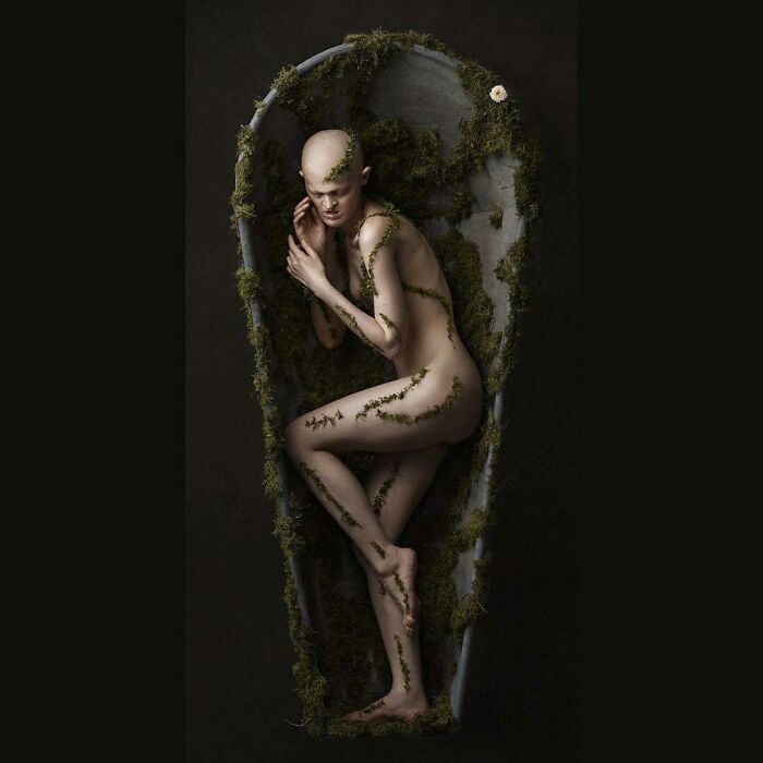 Unique model in nature-themed artistic pose, adorned with leaves in a cocoon-like setting.