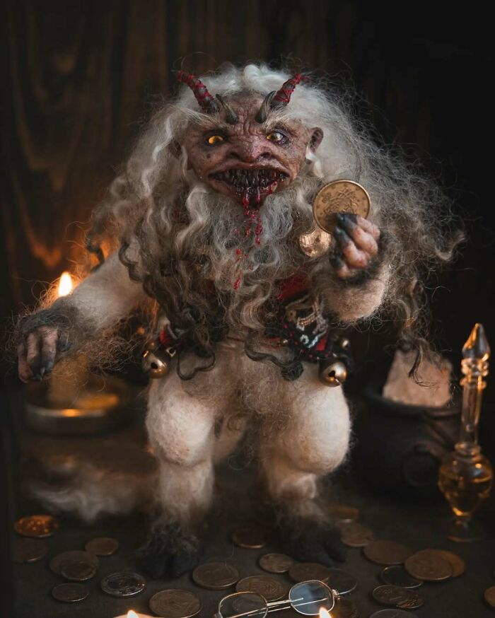 Creepy handmade doll with horns and long hair, holding a coin amid scattered coins and candlelight in a dark setting.