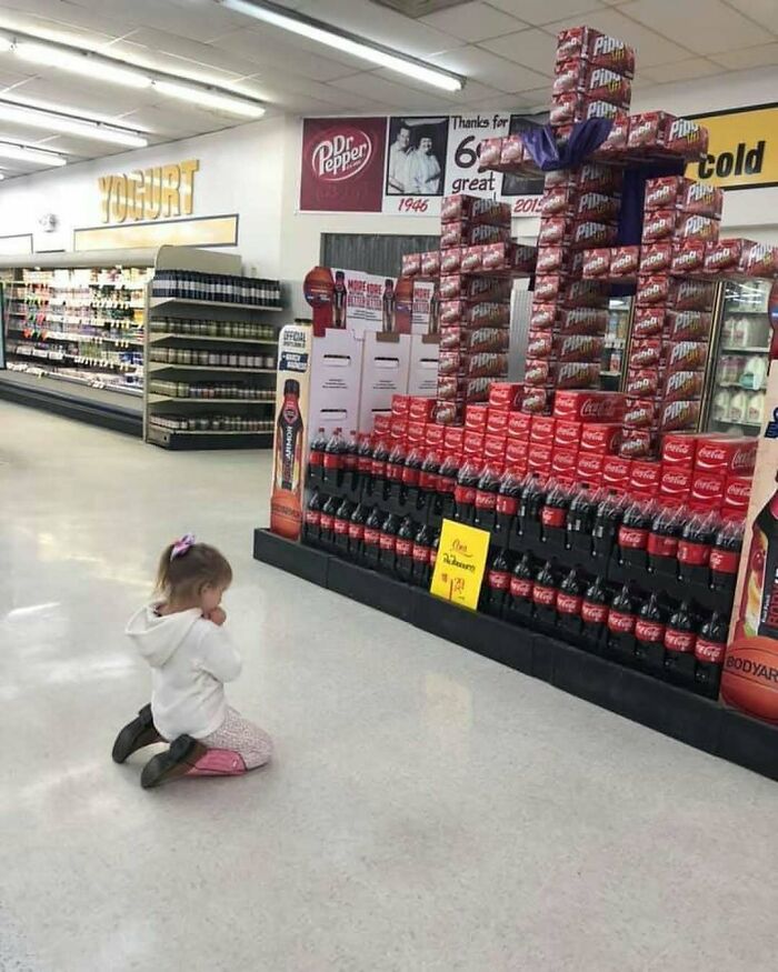 Child kneeling before soda display in grocery store, showcasing the strange nature of the internet.