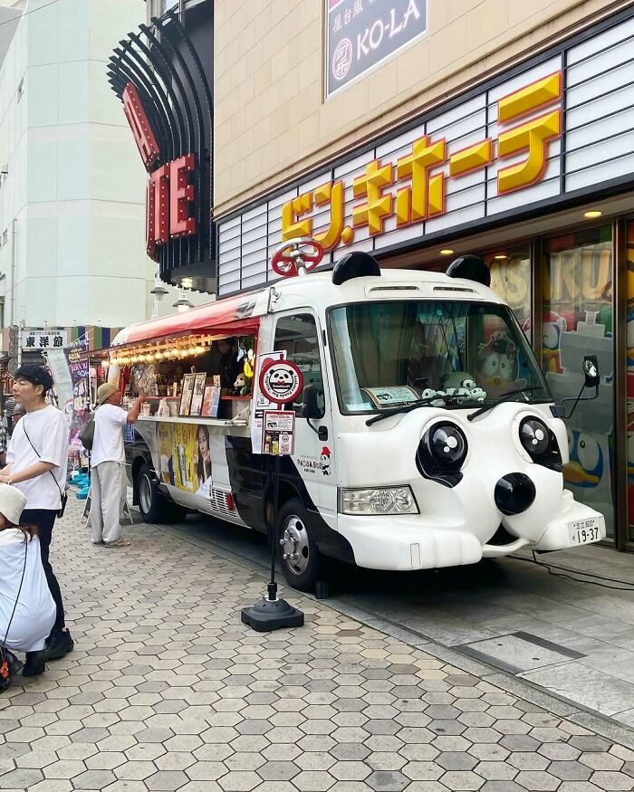 A panda-themed food truck on a bustling street in Japan, attracting curious visitors.