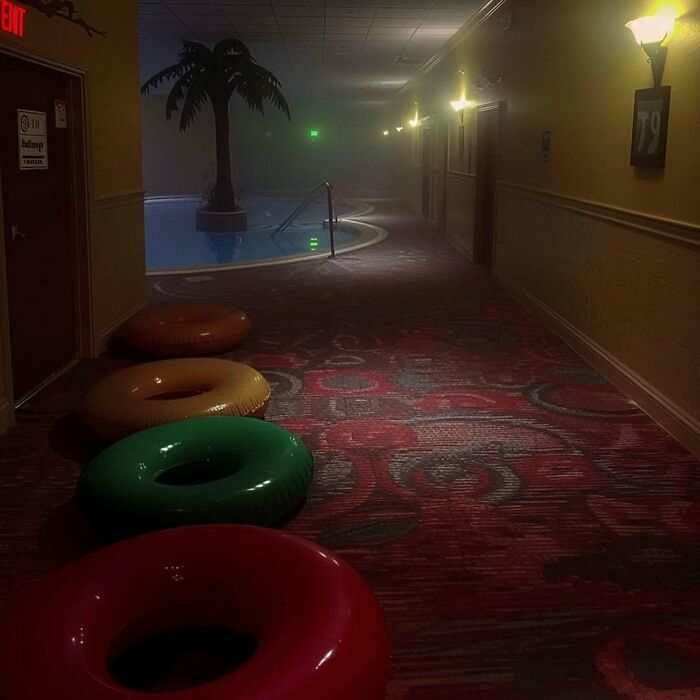 Dimly lit corridor with pool, float tubes, and palm tree sculpture; an eerie liminal space.