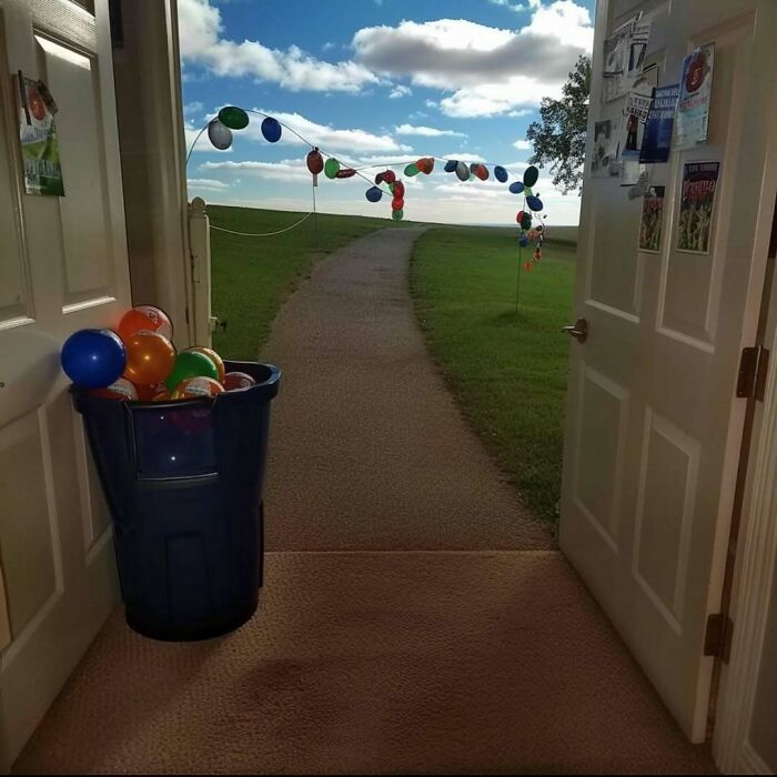 Open doors leading to a path adorned with balloons, creating a liminal space under a blue sky with clouds.
