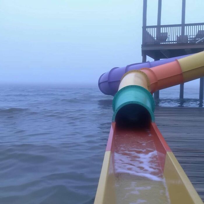 Colorful waterslide extending into foggy waters, creating a liminal space.