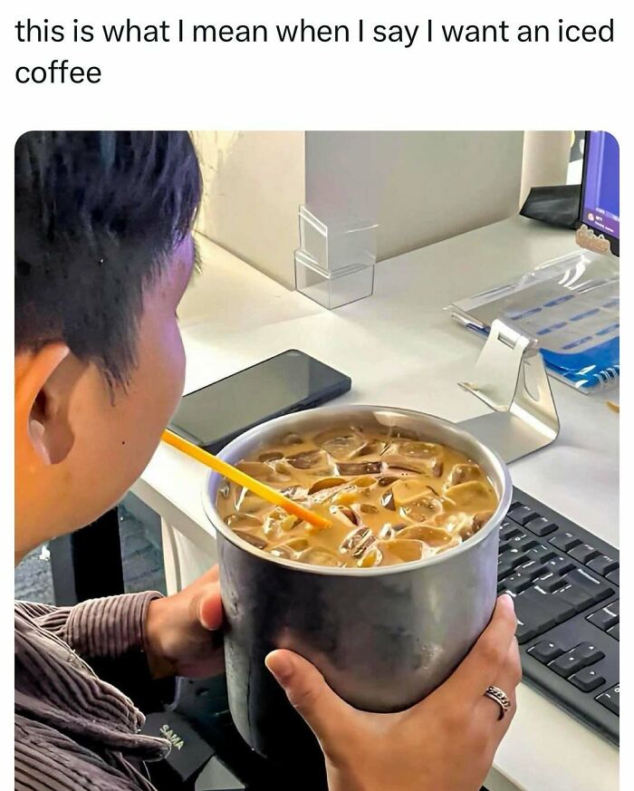 Person holding large bucket of iced coffee with straw near a computer, showcasing funny college confession meme.