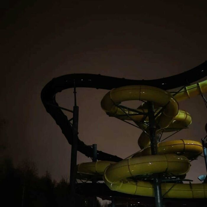 Dark liminal space featuring an eerie, deserted waterslide spiraling under a cloudy night sky.