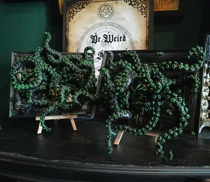 Creepy handmade crafts with green tentacles emerging from dark frames on display.