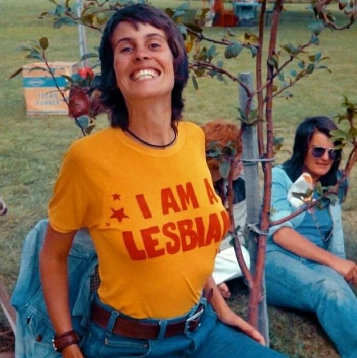 Person smiling in a yellow shirt with "I am a lesbian" text, capturing true happiness in an outdoor setting.