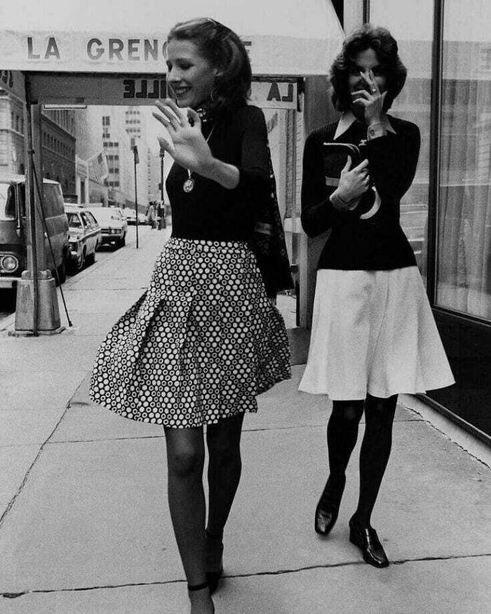 Two women smiling and walking on a city sidewalk, capturing true happiness in a candid moment.