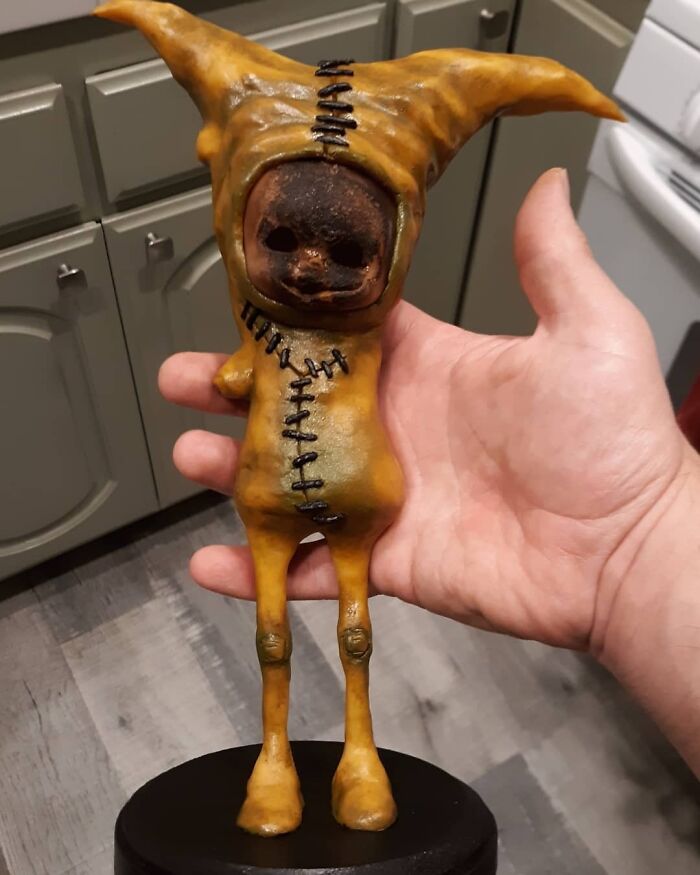 Hand holding a creepy handmade craft figure with stitched details and pointed ears.