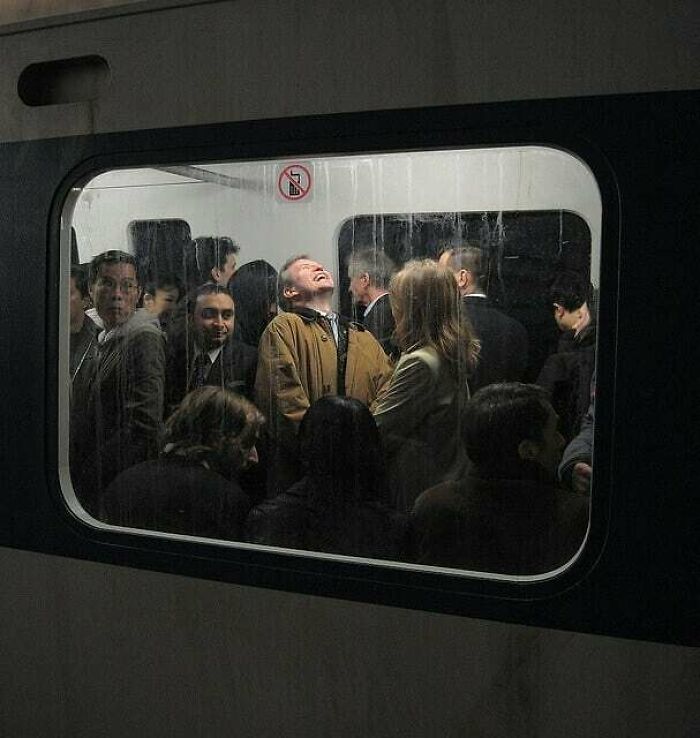 Person in a crowded train smiling with true happiness, surrounded by other commuters in dark attire.