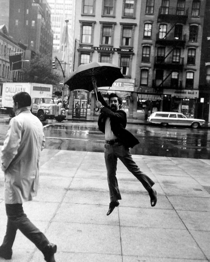 Man joyfully leaping with an umbrella on a rainy city street, capturing true happiness.