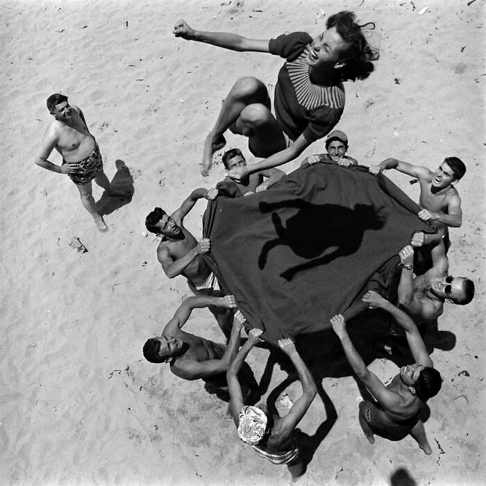 Group of people on a beach joyfully tossing a woman into the air, capturing true happiness.