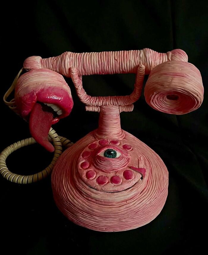 Creepy handmade craft of a vintage telephone with a tongue and eye on a dark background.