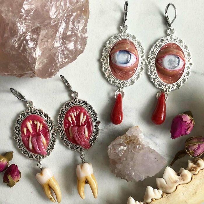 Creepy handmade crafts featuring earrings with eyes, fangs, and teeth surrounded by crystals and flowers.