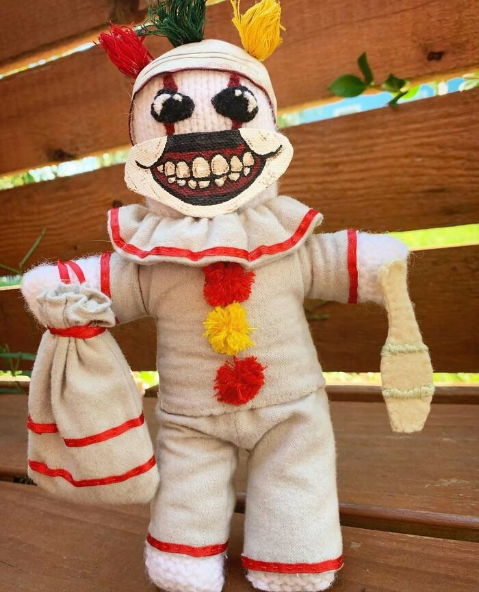 Creepy handmade craft of a clown doll with a painted smile and colorful pom-poms, standing against a wooden background.