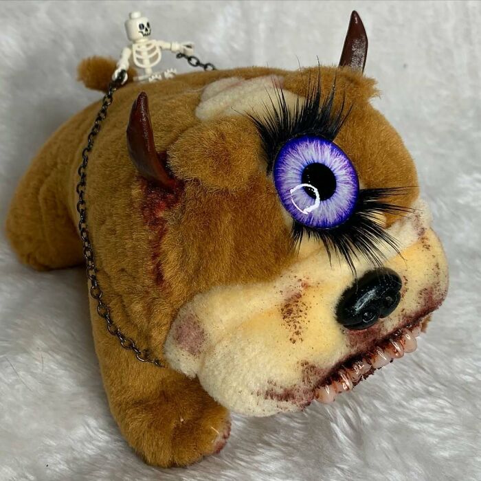 Creepy handmade craft of a plush creature with a large purple eye, horns, and skeletal figure on its back.