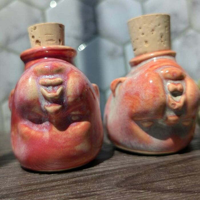 Two eerie handmade ceramic crafts with faces and cork tops on a wooden surface.