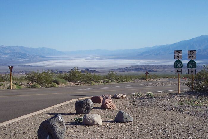 Desert road with signs for Route 190, showcasing legendary American road routes under a clear blue sky and mountains.