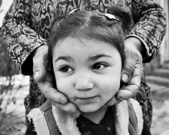Black and white photo of a child, with hands gently cupping their face, symbolizing childhood innocence and resilience.