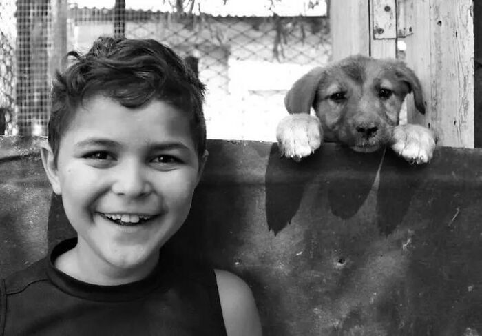 A child smiling next to a puppy in a black and white photograph, illustrating childhood innocence and resilience.