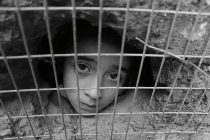 Child peering through a fence, symbolizing the innocence and resilience captured in black and white photography.