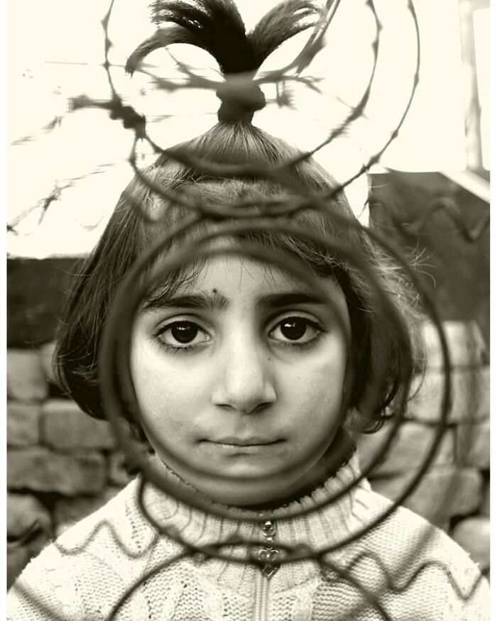 Child framed by wires in a black and white photo, showcasing childhood innocence and resilience.