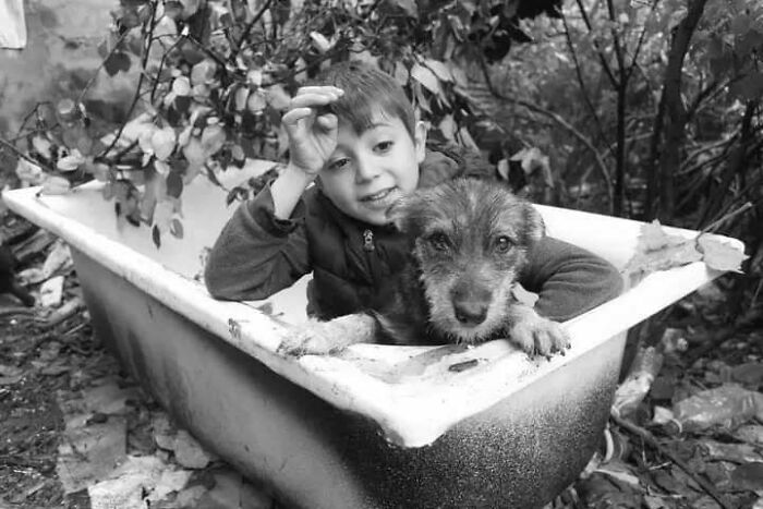 Childhood moment: A child and a dog in a tub, showcasing innocence and resilience in black and white photography.