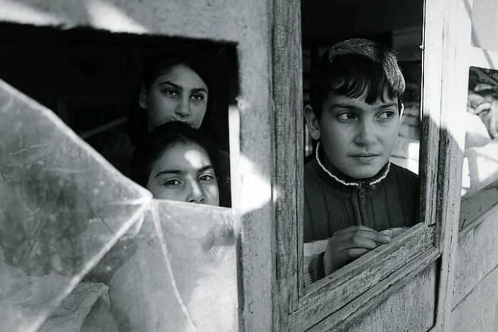 Children look out from behind a c*****d window in a black and white photo, capturing innocence and resilience.