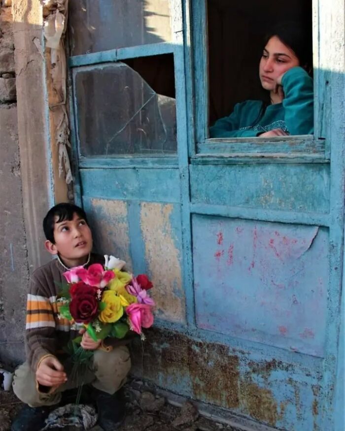 Child holding colorful flowers in front of a broken window, capturing childhood's innocence and resilience.