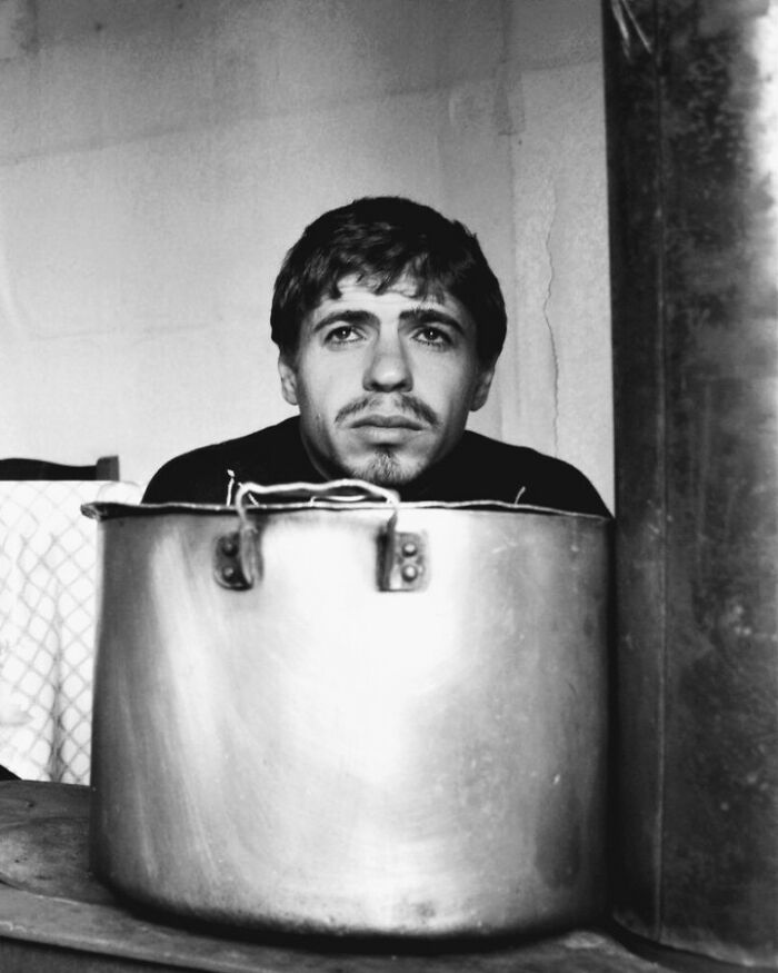 Black and white photo of a young man behind a large pot, conveying childhood's resilience and innocence.