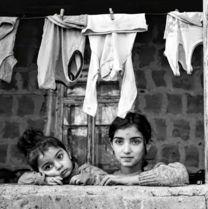 Black and white photo of two children in a window, with laundry hanging above, showcasing childhood innocence and resilience.