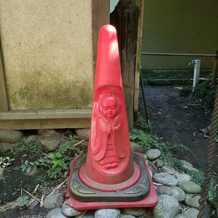 Red traffic cone with a carved figure, blending tradition and modernity in an intriguing Japanese setting.