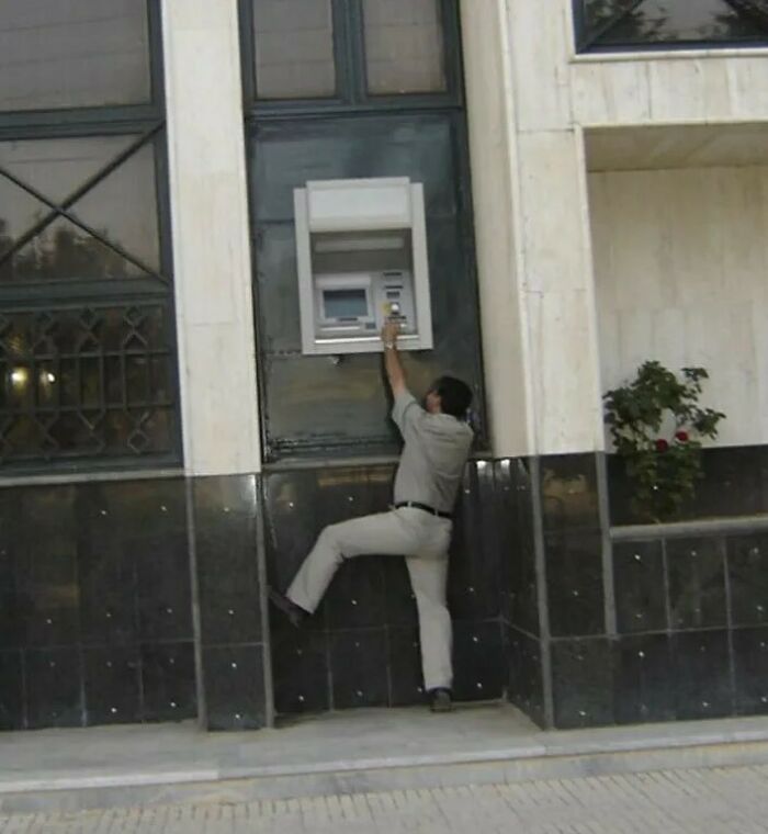 A man reaching for a high ATM, showcasing a design fail.