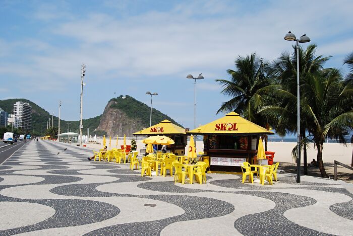 Retro Brazilian beach scene with yellow chairs and palm trees by the sea, showcasing classic sun and sand vibes.