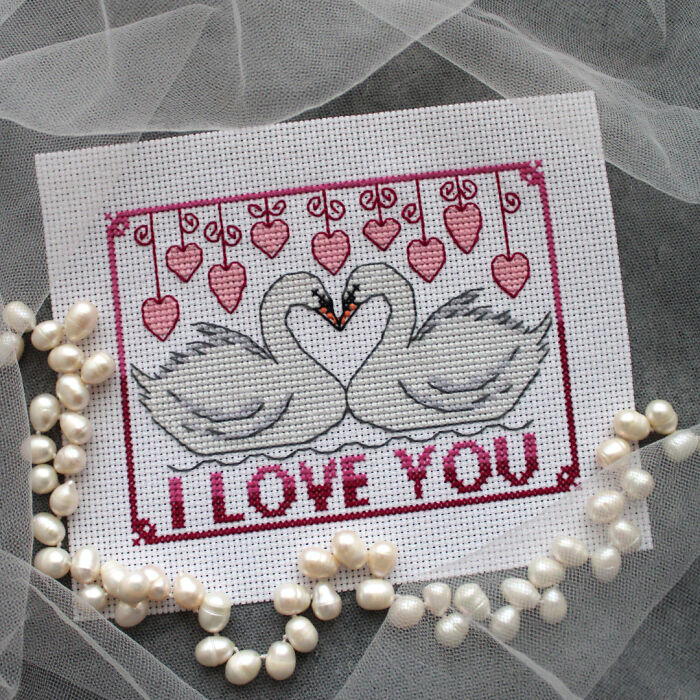 Cross stitch pattern with swans and hearts, featuring "I Love You" text. Pearls and tulle adorn the design.