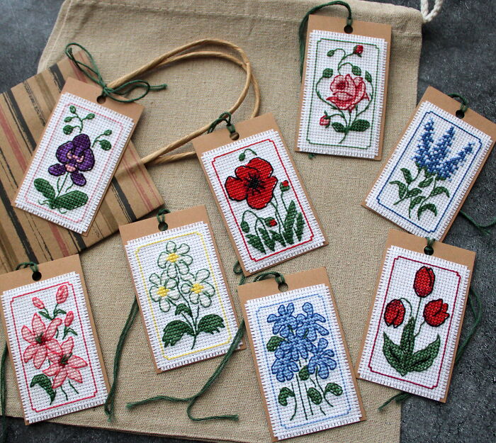 Digital cross stitch patterns featuring various floral designs on tags, arranged on a textured background.