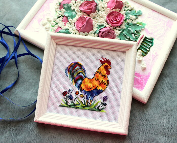 Framed digital cross stitch pattern of a colorful rooster with floral background.