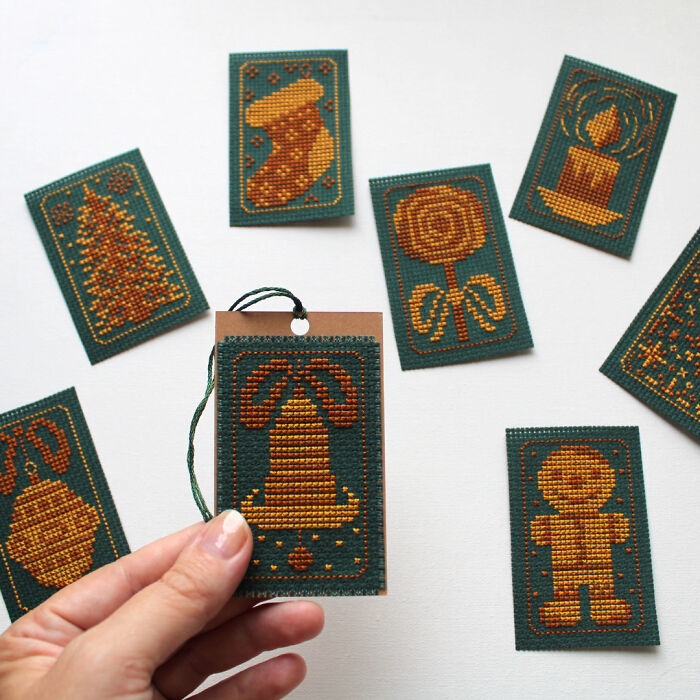Hand holding a small cross stitch pattern card with holiday designs and green background.