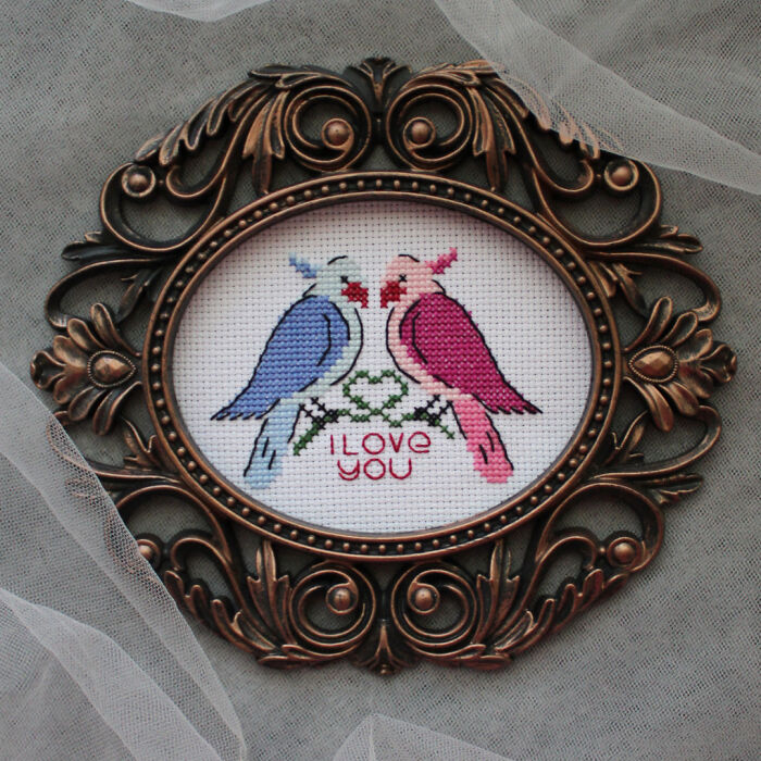 Two lovebirds cross stitch pattern in an ornate frame, designed by a digital cross stitch pattern designer.