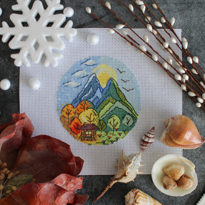 Digital cross stitch pattern of a mountain scene surrounded by seashells and decorative accents.