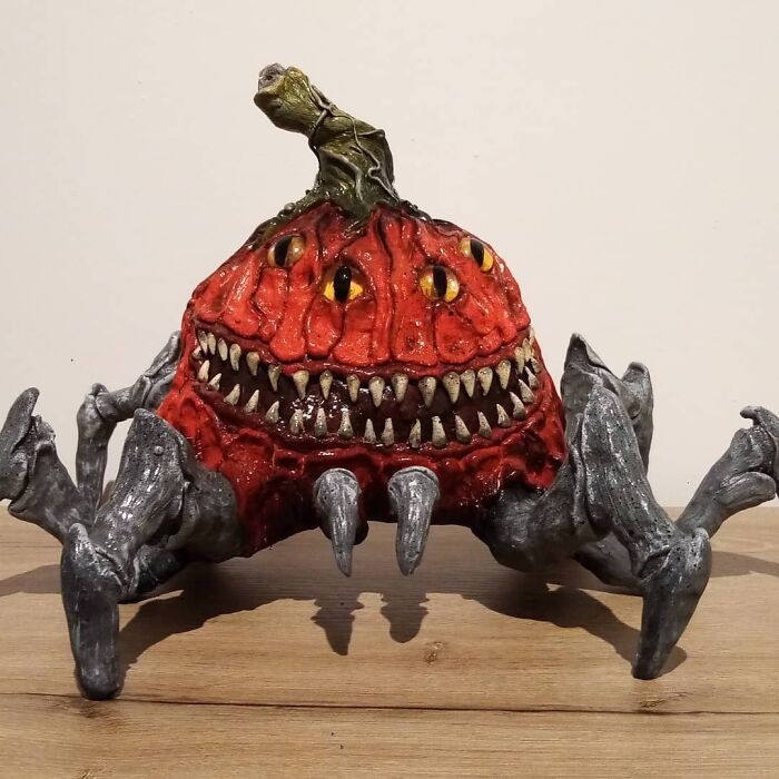 Creepy handmade craft of a spider-like creature with a pumpkin head and sharp teeth on a wooden surface.