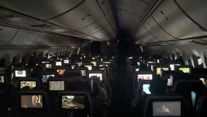 Airplane interior at night with lit screens, showcasing the strange atmosphere of the internet age.