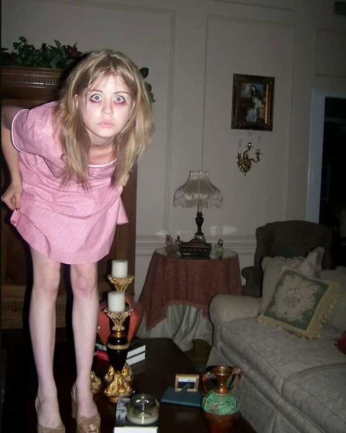 A person with wide eyes in a living room, standing on a table, exemplifying strange internet content.